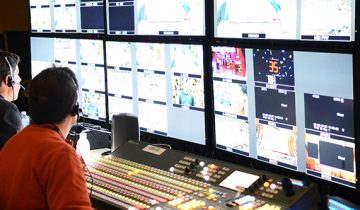 two men with headsets sitting and looking at multiple screens at broadcast work station
