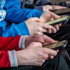Young people's hands holding cell phones. One is wearing red and the other blue.