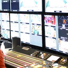 two men with headsets sitting and looking at multiple screens at broadcast work station